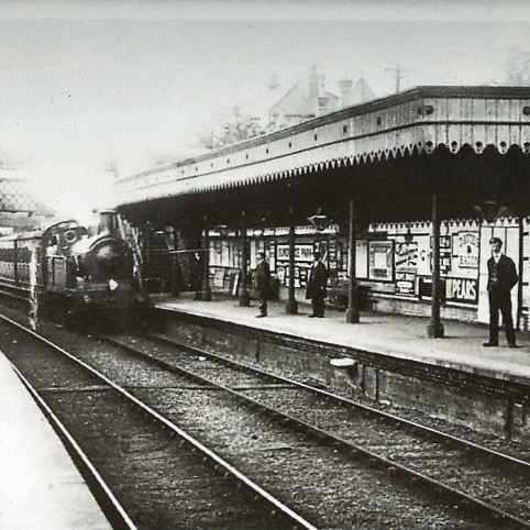 A black-and-white photo of a steam train pulling into a station platform.